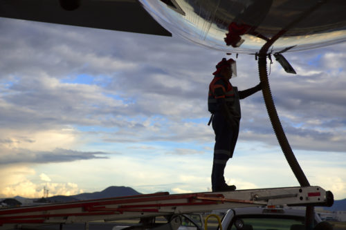 Airport staff operator refueling aircraft against blue sky